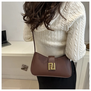 Detail of a brown leather shoulder bag with a gold geometric clasp on a white sweater