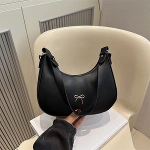 Detail of black hobo bag with a silver metal bow and wide leather shoulder strap
