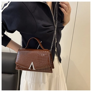 Detail of dark brown crocodile embossed leather handbag with silver V-shaped buckle clasp