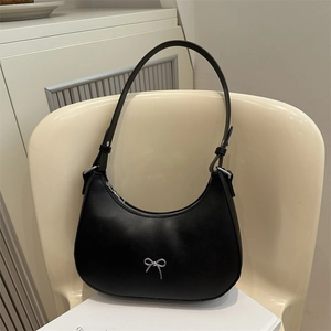 Close-up of black leather hobo bag with a silver bow ornament on a beige seat