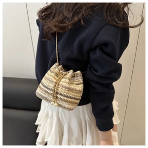 Detail of woven bucket bag featuring striped texture, gold chain and pearl drawstring