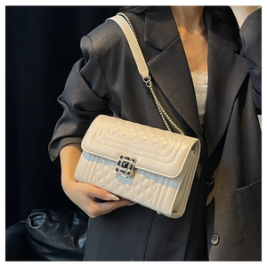 Detail of off-white quilted crossbody bag with black gemstone buckle and chain strap