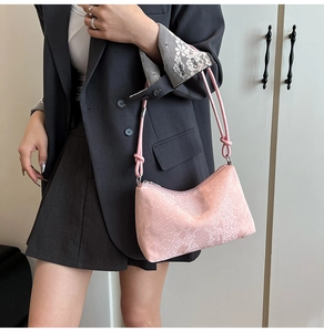 Close-up of pink crescent underarm bag with snake skin texture on model with black suit