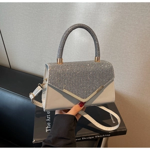 Detailed view of silver rhinestones and V-shaped gold metal frame on a white leather bag