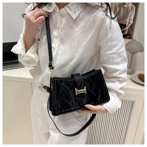 Detail of a pleated black baguette bag with a golden H-buckle on a white linen shirt
