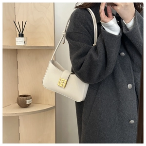 Detail of white leather shoulder bag with gold geometric clasp on wooden background