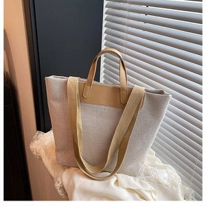 Close-up of the beige canvas tote bag showing camel leather trim and a wide fabric strap