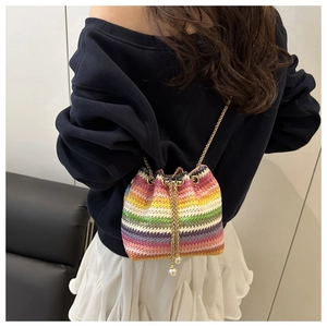 Detail of colorful woven bucket bag featuring gold chain and white pearl drawstring charms