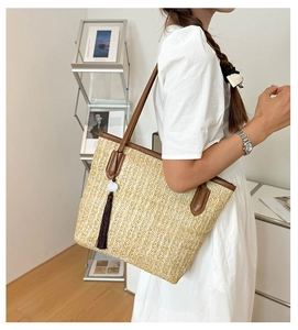 Close-up of woven straw tote bag with brown leather trim and decorative tassel detail