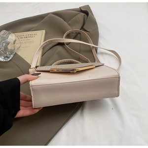 Detail view of cream crossbody bag with gold metal buckle and woven handle on white cloth