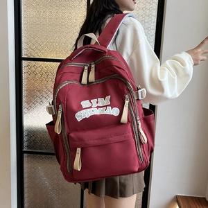 Burgundy nylon backpack with SJM SIJIMIAO lettering and long zipper pulls on model