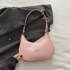 Detail of pink faux leather crescent bag featuring a silver bow and adjustable strap