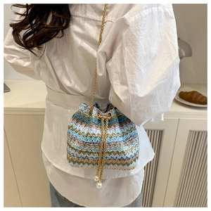 Detail of colorful woven bucket bag featuring gold chain strap and pearl drawstring charms