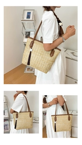 Detail of a woven straw tote bag featuring brown leather straps and a tassel charm