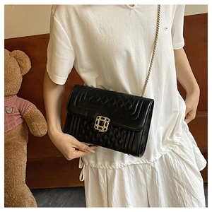 Close-up of black quilted crossbody bag featuring a golden buckle and metal chain strap