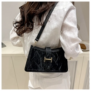 Detail of a black pleated baguette bag with a gold clasp worn by a model in a minimalist setting
