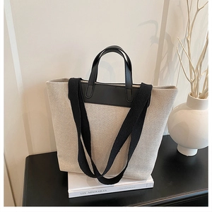 Detail of a large canvas tote bag with black leather handles on a minimalist shelf