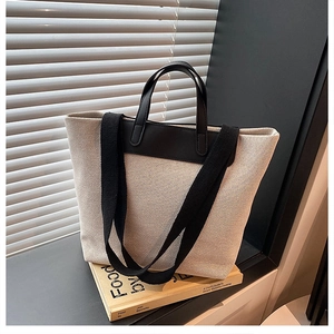 Detail of large canvas tote bag showing black leather handles and wide shoulder strap