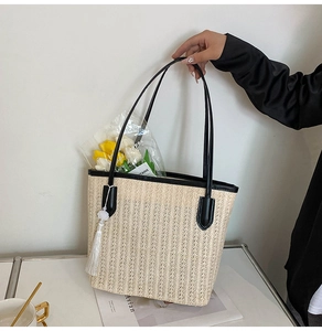 Detail of large straw tote bag featuring black leather handles and white silk tassel