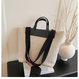 Detail of minimalist cream canvas tote bag featuring black contrast handles and shoulder strap