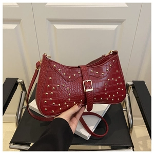 Vue détaillée de la texture crocodile rouge foncé et des clous dorés du sac croissant
