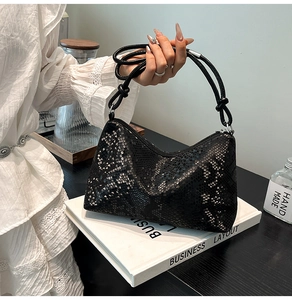 Detail of black snake embossed hobo bag with zip closure and knotted strap held by model