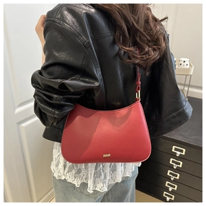 Close-up of red matte leather crescent bag featuring a gold logo and adjustable strap
