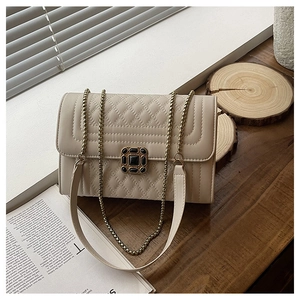 Close-up of beige quilted crossbody bag with ornate gold buckle on wooden surface