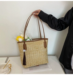 Close-up of woven straw tote bag with brown leather trim and decorative tassel details