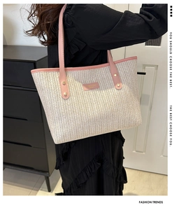 Detail of woven straw tote bag featuring pink leather trim and metallic brand plaque