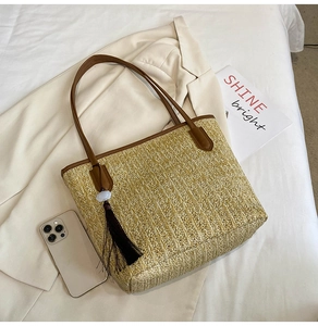 Detail of woven straw tote bag with brown leather handles and a tassel cloud charm