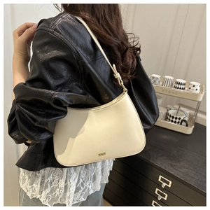 Close-up of cream underarm bag with gold metal logo and sleek crescent silhouette