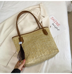 Detail of a woven straw tote with brown leather handles and a long purple tassel pendant