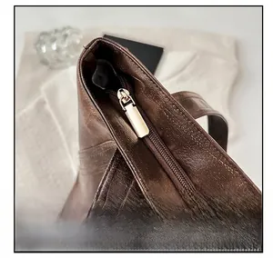 Detail view of a dark brown leather tote bag with a gold metal zipper and smooth texture