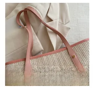 Detail of woven straw tote bag with pink leather handle and gold rivet reinforcement