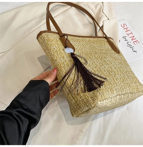 Detail of hand-woven straw tote bag featuring brown leather straps and stylish tassel charm
