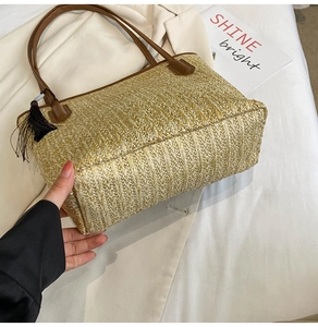Detail of woven straw tote bag with brown leather handles and black silk tassel accessory