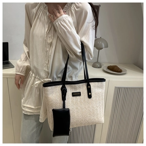 Detail of a beige woven straw tote bag with black contrast trim and a stylish small pouch