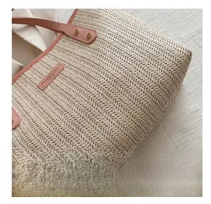 Close-up of beige woven straw tote with pink leather handles and branded logo tag