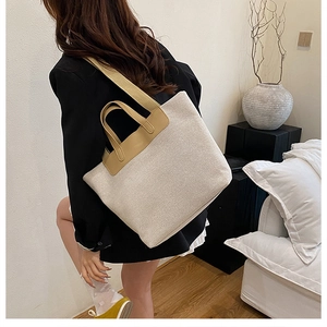 Close-up of contrast leather trim on a large cream canvas tote bag worn by a model