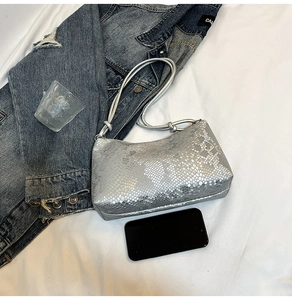 Detailed view of silver snakeskin textured shoulder bag on white fabric background