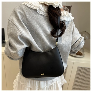 Detail of black leather underarm bag with gold metal letters worn by a model in a room