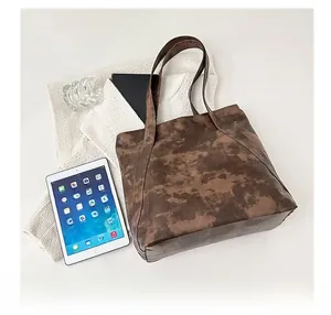 Overhead view of large dark brown tote bag with distressed faux leather texture on white desk