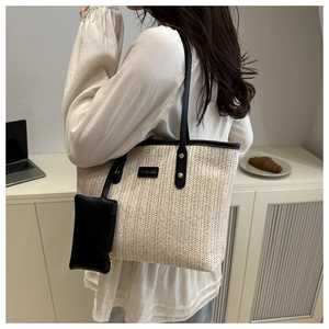Detail of contrast woven straw tote bag featuring long black straps and a mini zipper pouch