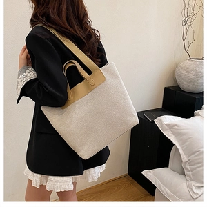 Close-up of beige canvas tote bag with brown leather straps shown on a model's shoulder