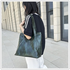 Detail of a large vintage dark green tote bag in glossy leather worn over the shoulder