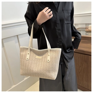 Detail of cream woven tote bag with white leather trim and metallic brand logo plate