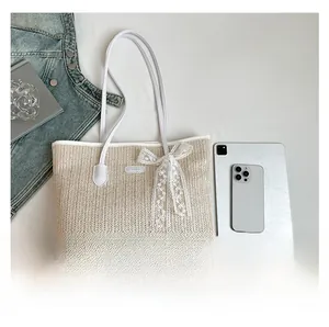 Détail d'un sac cabas en paille avec nœud en dentelle blanche et poignées en cuir