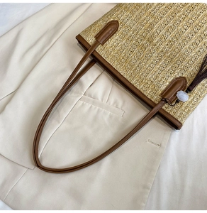 Detail of straw tote bag with brown leather handles and purple floral bead tassel charm