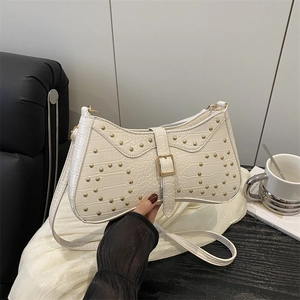 Sac baguette blanc à motif crocodile avec clous dorés et boucle, tenu à la main